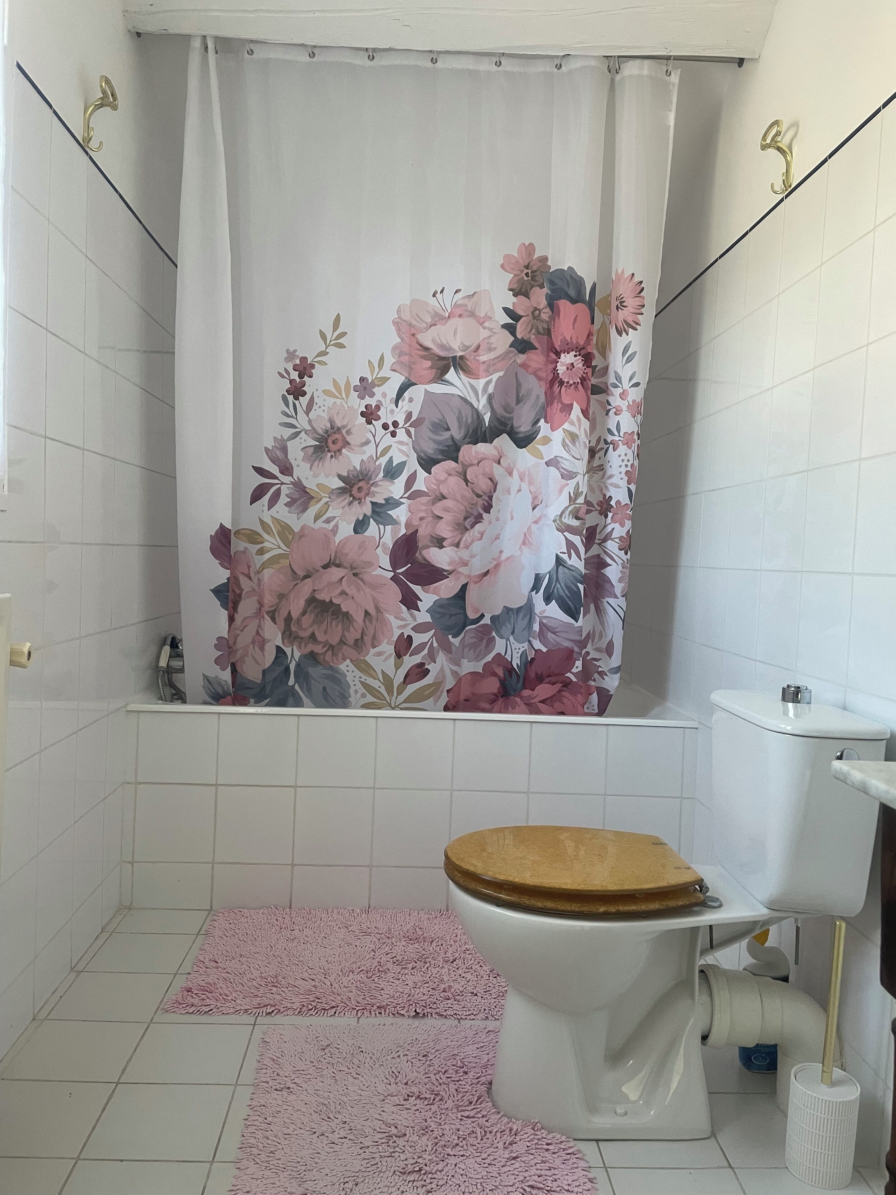 Een badkamer met een gordijn met bloemenprint, een houten toiletbril en roze vloerkleden.