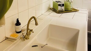 Keittiössä on valkoinen pesuallas, vihreä vedenkeitin ja leivänpaahdin tarjottimella.