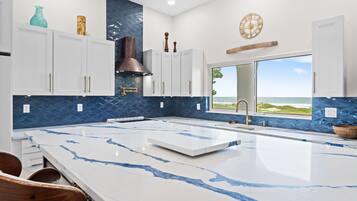 A modern kitchen with a large island, white cabinets, blue backsplash, and a view of the ocean.