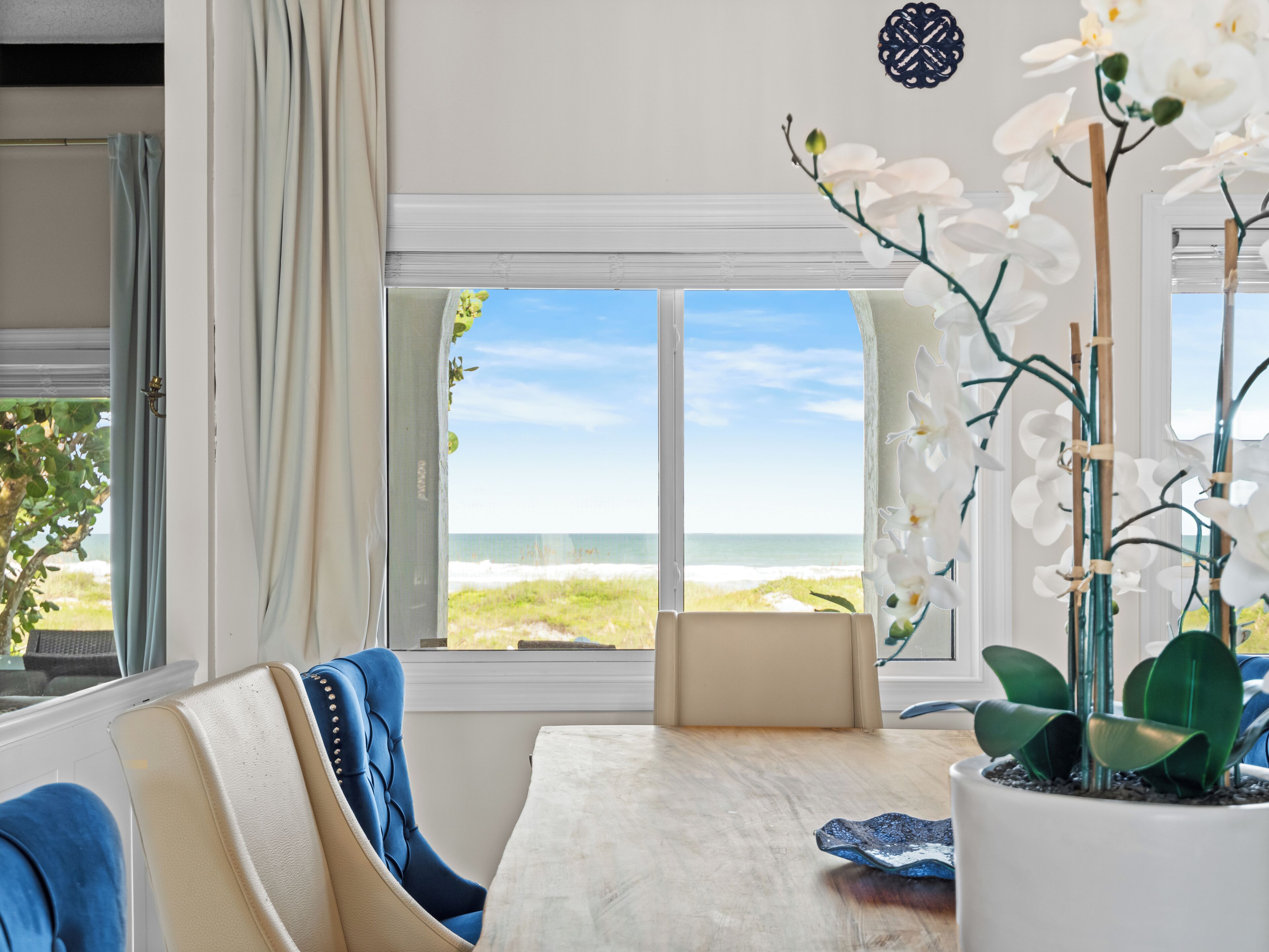 A room with a view of the beach, a potted orchid, a blue chair, and a table.