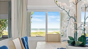A room with a view of the beach, a potted orchid, a blue chair, and a table.