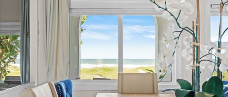 A room with a view of the beach, a potted orchid, a blue chair, and a table.
