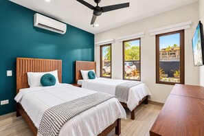A hotel room with two beds, a ceiling fan, an air conditioning unit, and a view of the outside.
