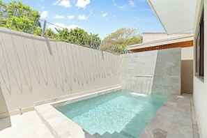 Una piscina con una cascada, rodeada de un muro de piedra y una cerca blanca.