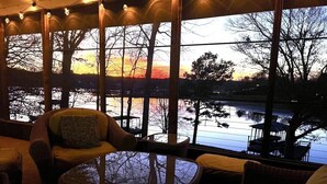 A cozy room with a large window overlooking a body of water and trees, furnished with wicker chairs and a glass table.