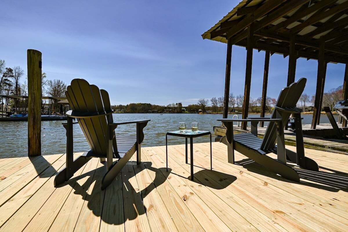 A wooden deck with two Adirondack chairs and a small table with two glasses, overlooking a body of water.