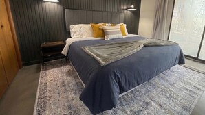 A bedroom with a bed, nightstands, a patterned rug, and a large window with curtains.