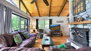 A cozy living room with a wooden ceiling, a stone fireplace, a television, and a comfortable seating area.