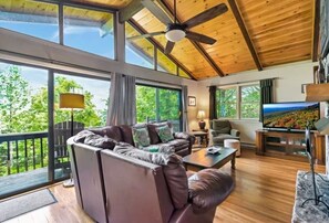 Amplia sala de estar con un sofá de cuero grande, una mesa de centro y un televisor. Amplias ventanas ofrecen vistas al exterior.