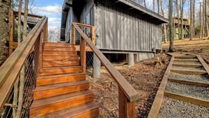 A wooden staircase leading to a cabin with a metal railing, surrounded by trees and gravel.