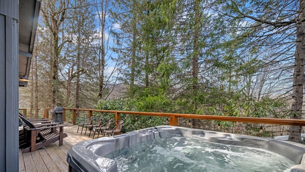 A hot tub on a wooden deck with a wooden railing, surrounded by trees.