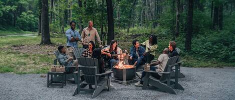 A group of people seated around a fire pit in a forested area.