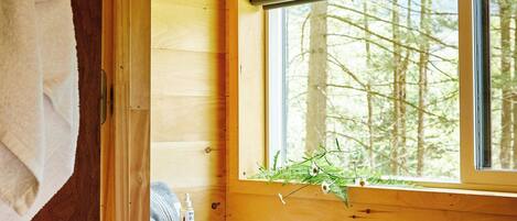 A wooden cabin bathroom with a toilet, a window, and a towel hanging on the wall.