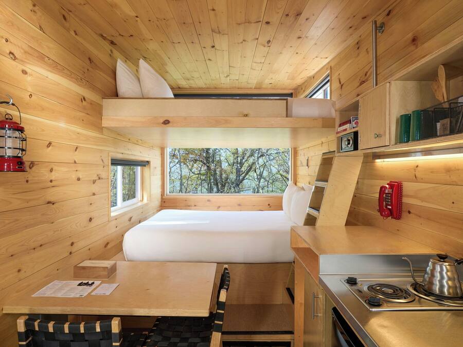 Une petite cabine comprenant un lit superposé, un coin cuisine et une fenêtre donnant sur la forêt.