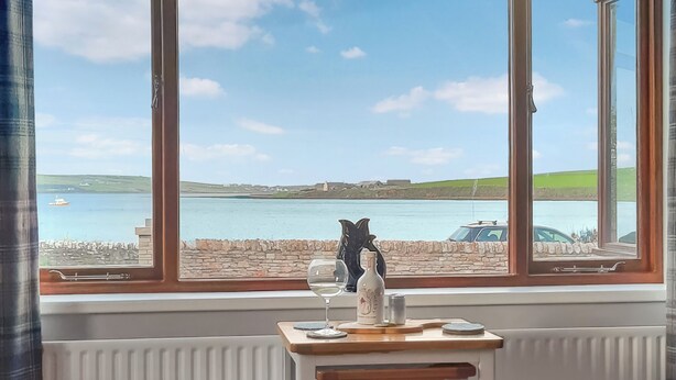 Une pièce avec vue sur un plan d’eau, un mur en pierre et une petite table sur laquelle se trouvent une bouteille et un verre.