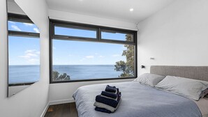 Un dormitorio con una cama grande, dos ventanas vistas al océano y una cama bien hecha con toallas dobladas.
