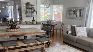 Un salón amplio con una mesa de comedor de madera, bancos acolchados, un sofá gris y una alfombra estampada.