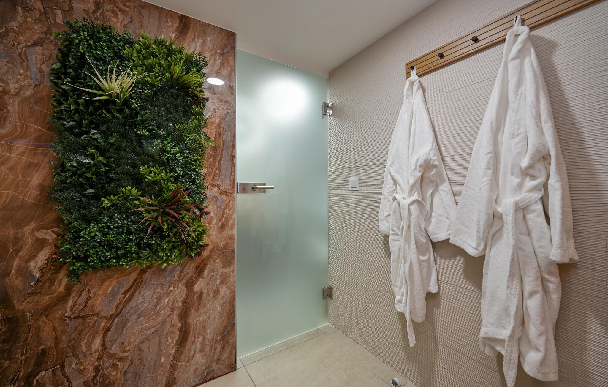 Un bagno con porta in vetro, un giardino verticale verde e asciugamani bianchi su un portasci legno.