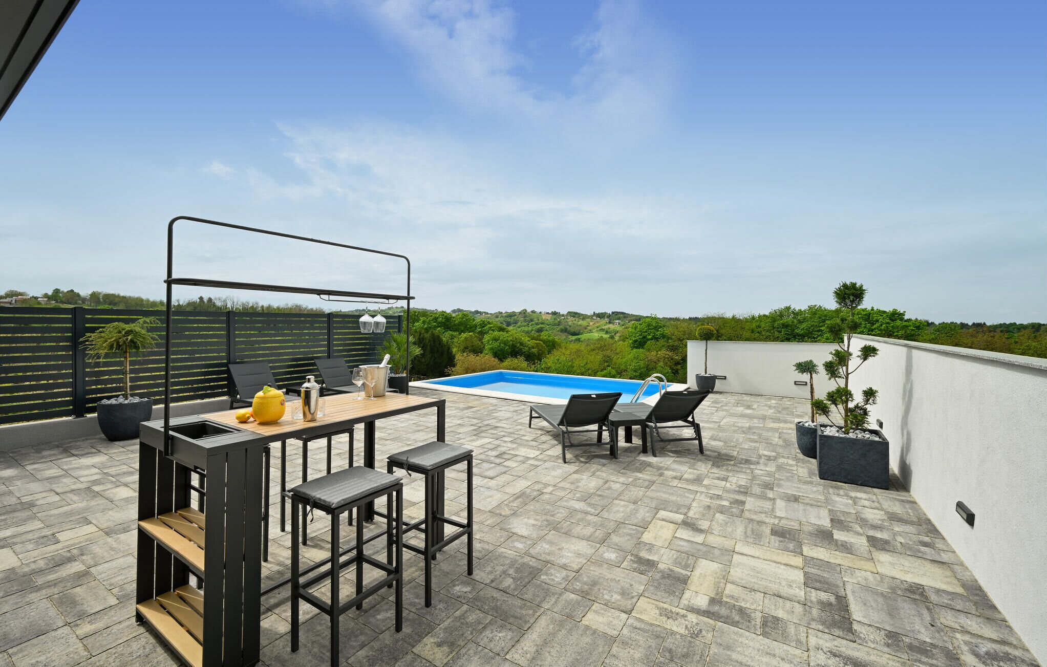 A rooftop patio with a pool, seating area, and a table with bar stools.