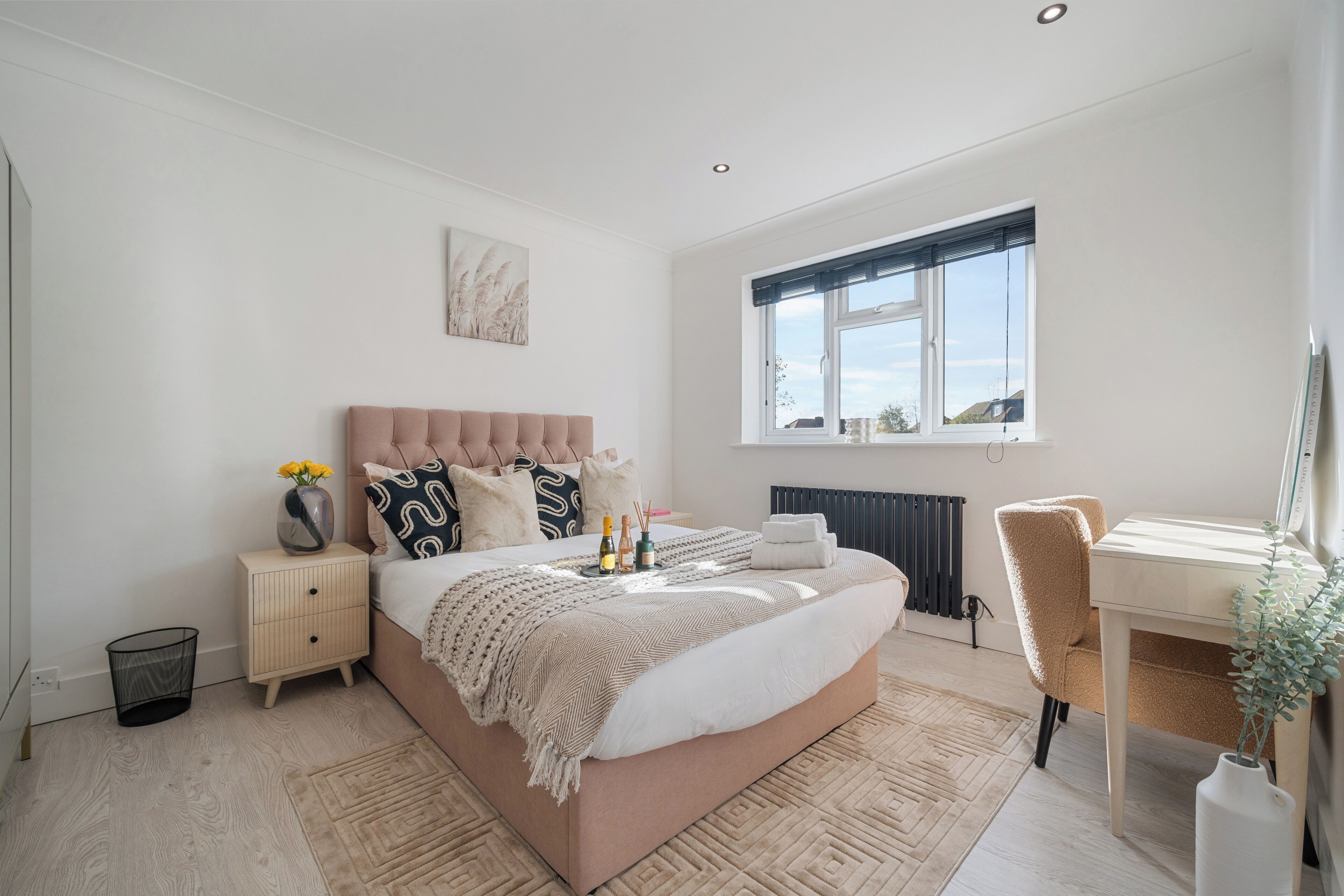 A bedroom with a large bed, bedside tables, a desk, and a window.