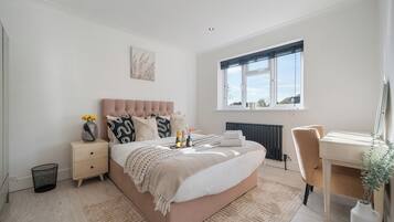 A bedroom with a large bed, bedside tables, a desk, and a window.