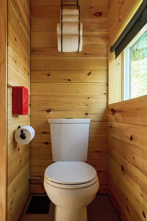 A wooden-paneled bathroom with a toilet, a red fire extinguisher, and a roll of toilet paper. - Postcard Cabins Beaver Creek, Outdoor Collection by Marriott Bonvoy (Lisbon)