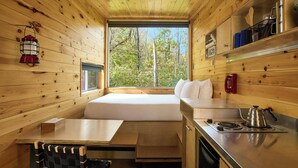 A cabin interior with a wooden interior, a window seat, a kitchenette, and a dining area. - Postcard Cabins Beaver Creek Ohio, Outdoor Collection by Marriott Bonvoy (Lisbon)