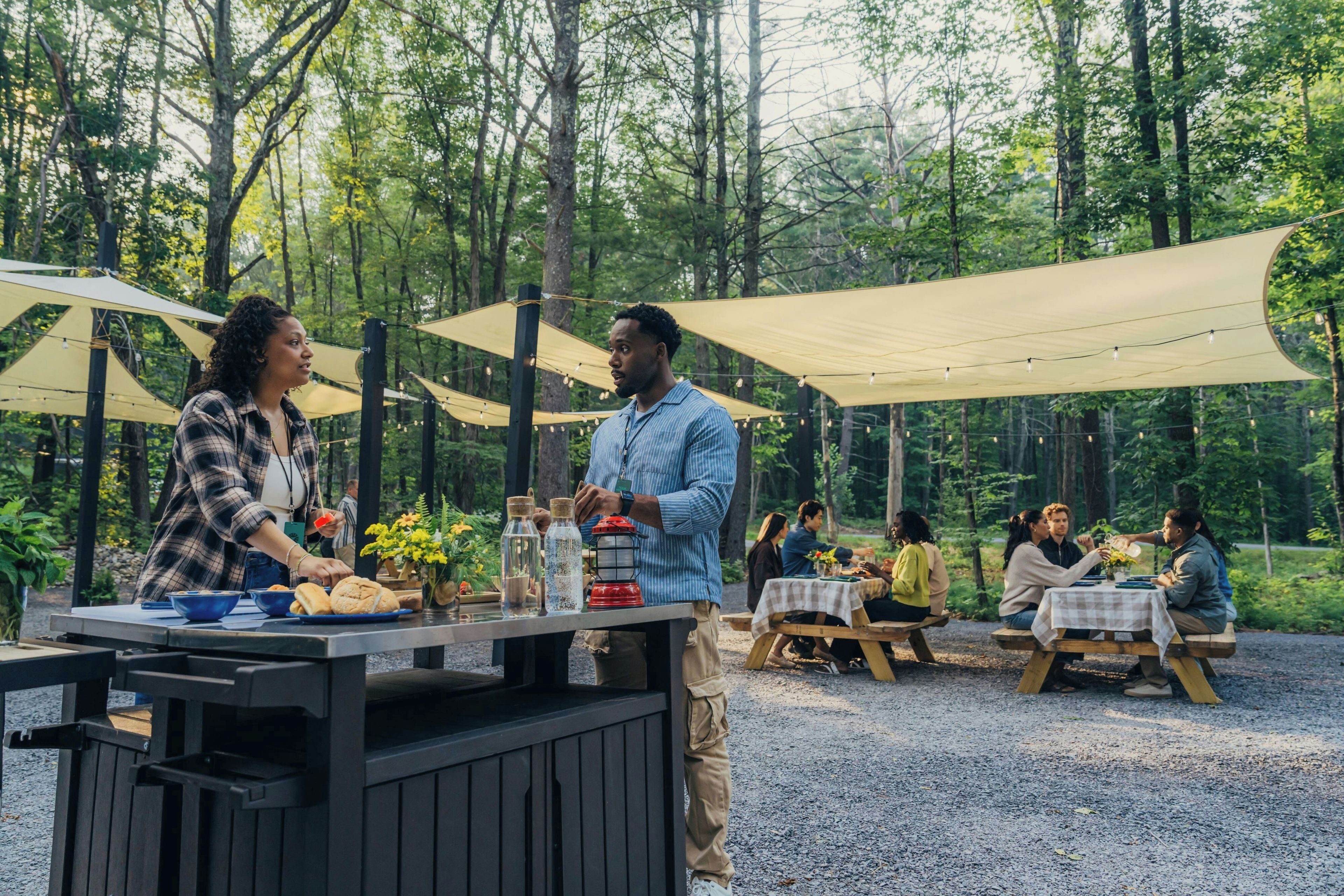 Un espace extérieur aménagé pour les repas, avec des tables et des chaises, entouré d’arbres.