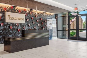 A reception desk with a sign reading 'The Crescendo,' a patterned wall, and a view of the outside through glass doors.