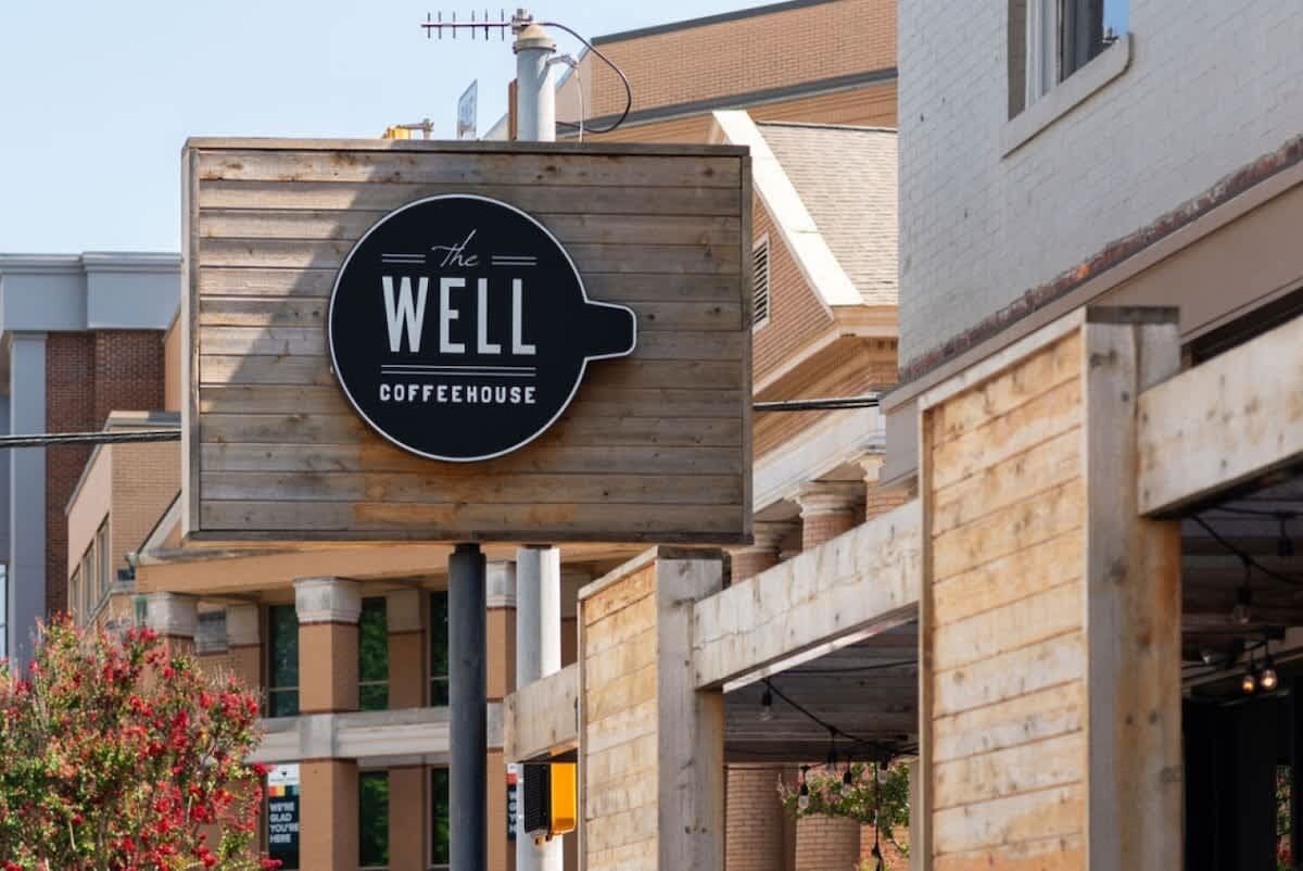 Une enseigne pour « The Well Coffeehouse », avec un fond en bois et un logo représentant une tasse de café.