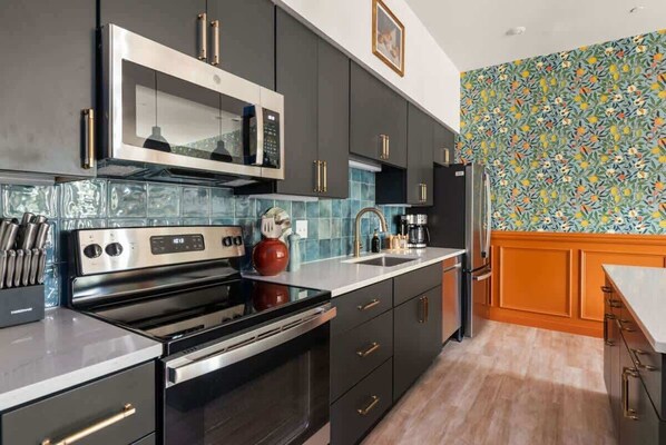 A modern kitchen with dark cabinetry, stainless steel appliances, and a colorful backsplash.