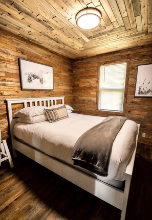 A bedroom with a wooden ceiling, a bed with white bedding, and two framed pictures on the walls. - Starry Night Cabin (Pacific County)