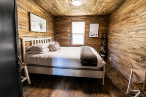 A wooden-paneled room with a bed, a window, and wall-mounted artwork.