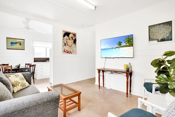 A living room with a sofa, a coffee table, a TV on the wall, and a plant.
