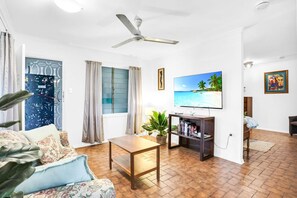 Un salon comprenant un téléviseur, un ventilateur de plafond, une table basse, un canapé, une bibliothèque et une plante.