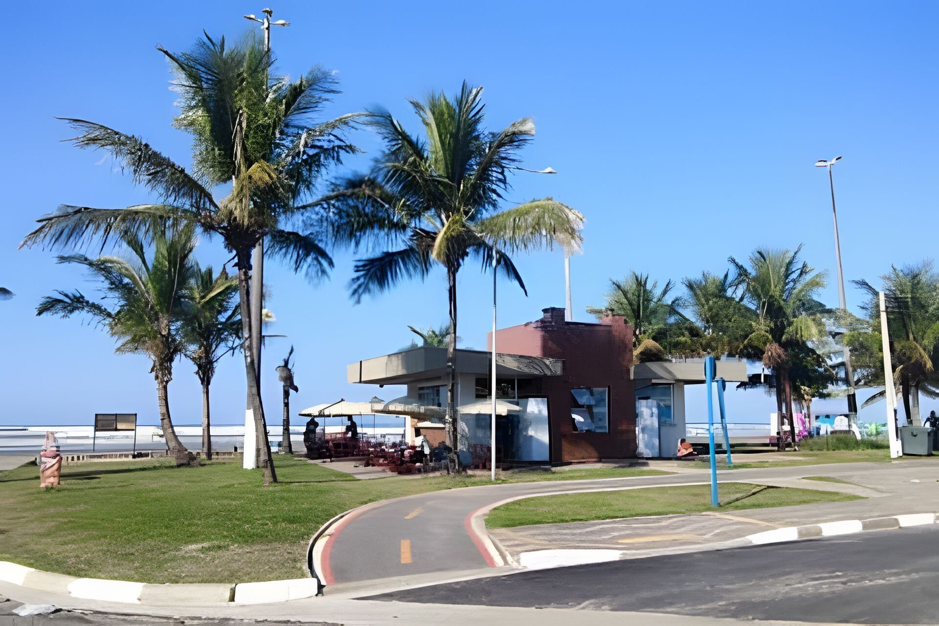 A building with a curved road in front, palm trees, and a clear sky.