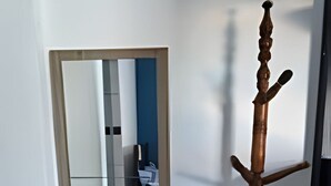 Un pasillo con un perchero, un espejo que refleja un baño y una puerta que da a otra habitación.