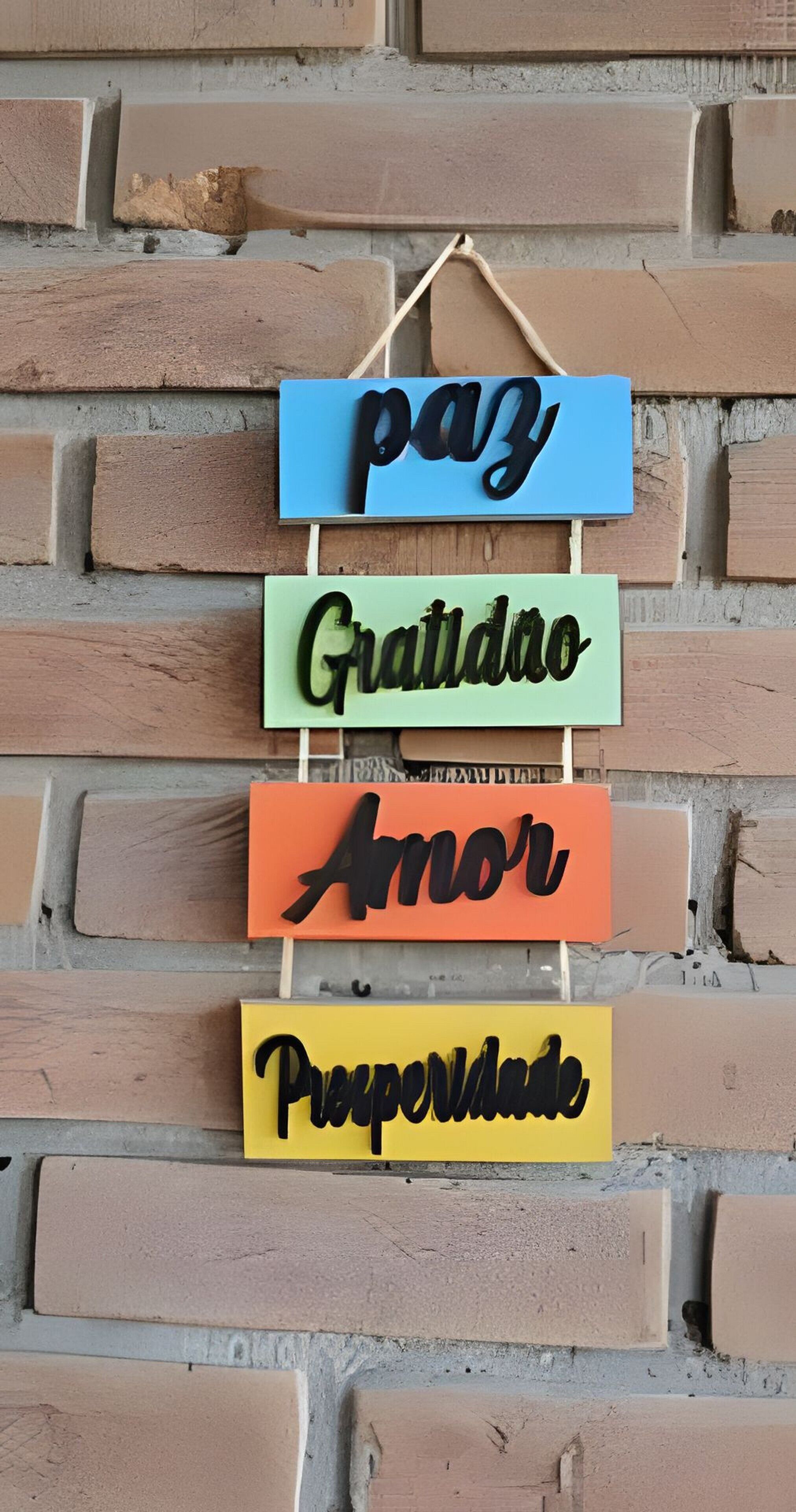 Eine Wand mit vier hängenden Schildern in verschiedenen Farben, jedes mit einem Wort in einer stilisierten Schrift.