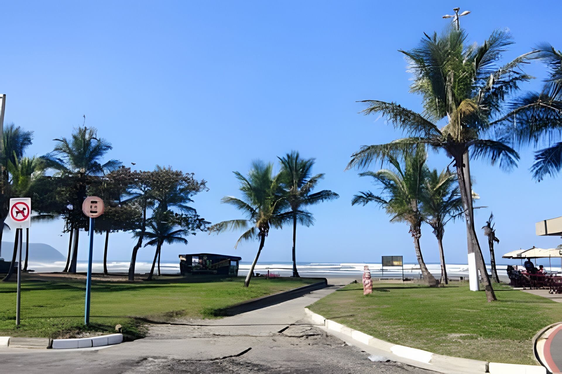 A beachside area with palm trees, a no parking sign, a small structure, and a view of the ocean.