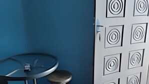 Una habitación con una pared azul, un televisor montado, una mesa redonda con dos taburetes y una puerta blanca decorada con diseños circulares.