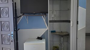 Una habitación compacta con un refrigerador blanco, un televisor montado, un lavamanos y un cubo de basura.