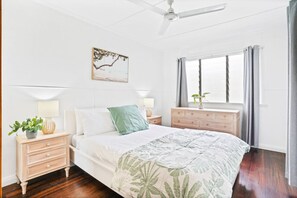 A bedroom with a bed, nightstands, a dresser, a ceiling fan, a window with curtains, and a wall-mounted picture.
