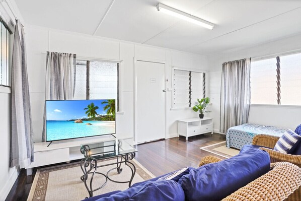 A modern living room with a flat-screen TV, a sofa, a small table, and a potted plant.