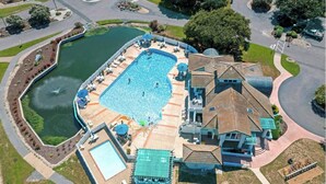 Ein Luftbild eines Anwesens mit großem Schwimmbad, Tennisplatz und einem Gebäude mit markanter Dachgestaltung.