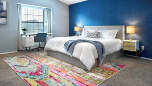 Une chambre à coucher avec un lit, des tables de chevet, un bureau et un tapis coloré.