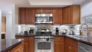 A modern kitchen with wooden cabinets, stainless steel appliances, and a tiled backsplash. - Hot Tub, Game Room, Fire Pit (Round Rock)