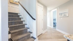 A staircase with carpeted steps and a handrail, leading to a hallway with a wooden floor and a door at the end. - Oceanside 7min walk2beach,6BR,Pool,HotTub,Foosball (Corolla)