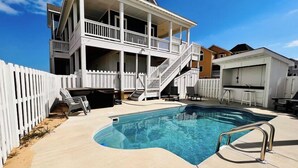 A two-story house with a pool, a white fence, and a covered outdoor area with chairs and a barbecue. - Oceanside 7min walk2beach,6BR,Pool,HotTub,Foosball (Corolla)