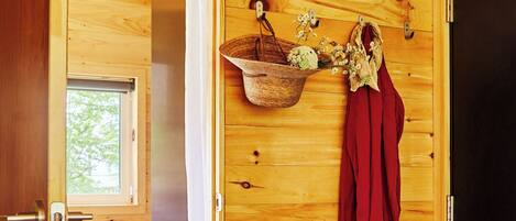 A wooden room with a shower, a small window, a basket with flowers, and a pair of shoes on the floor.