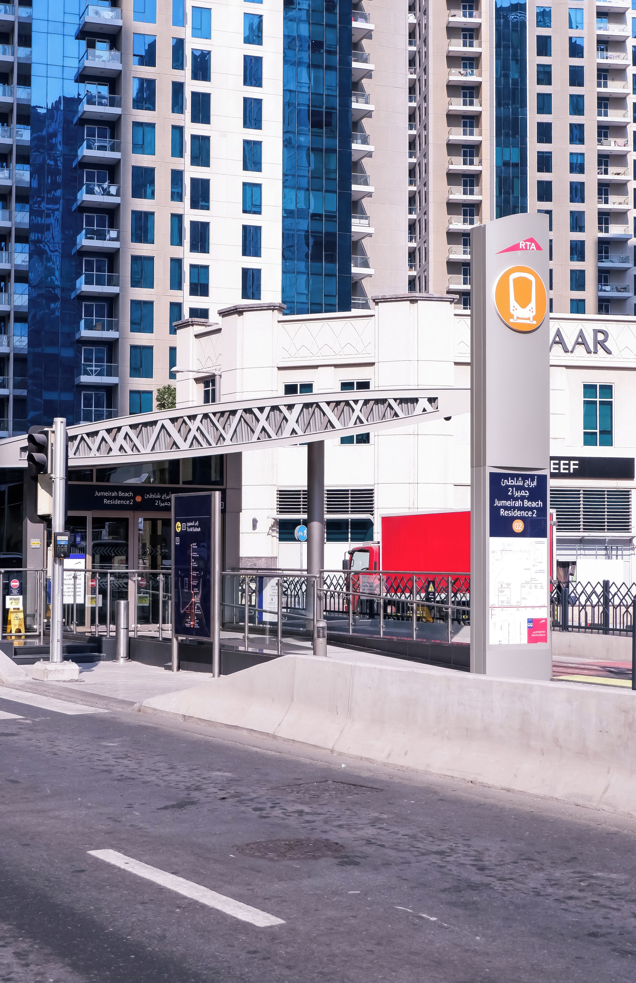 A modern building with a glass facade, a red truck parked in front, and a sign indicating a residential area.